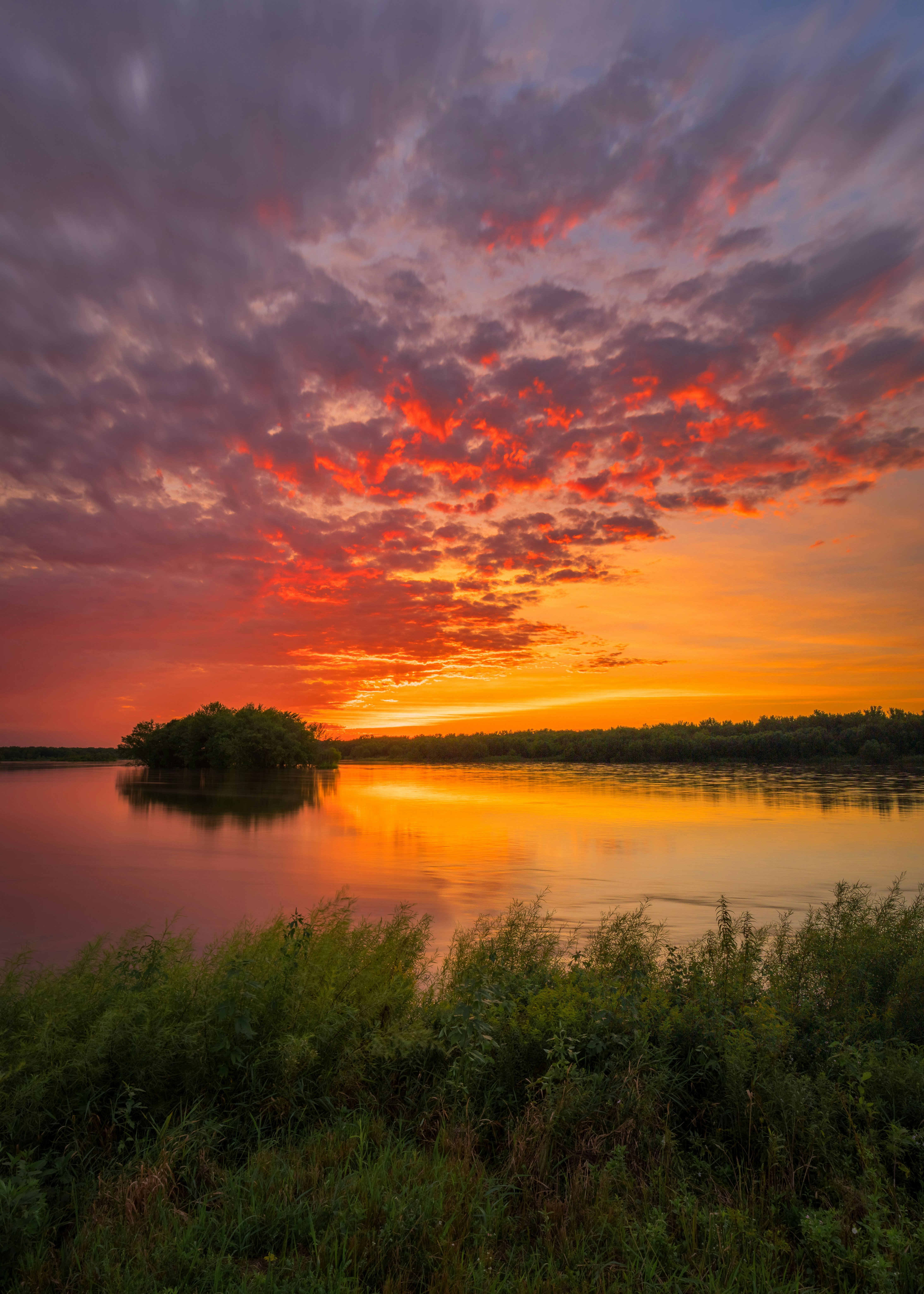 body of water near green grass field during sunset